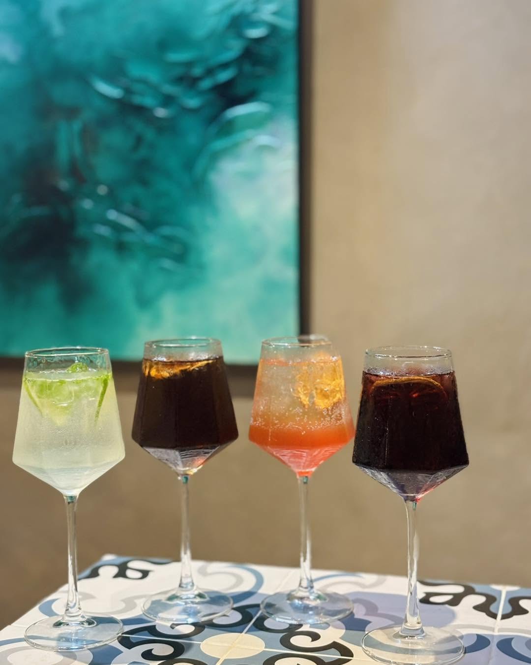 Four artisanal cocktails in faceted stemware against a teal painting