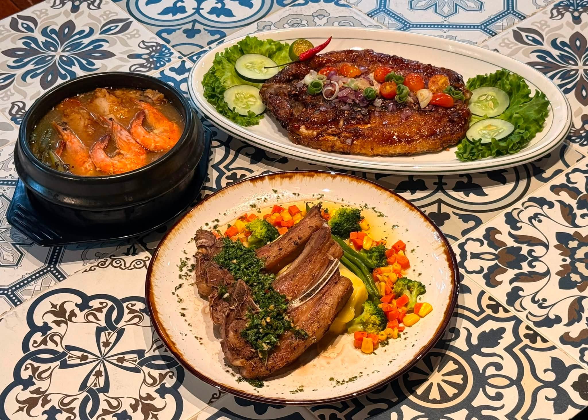 Steak, chops with chimichurri and a clay pot of prawns on Spanish tile
